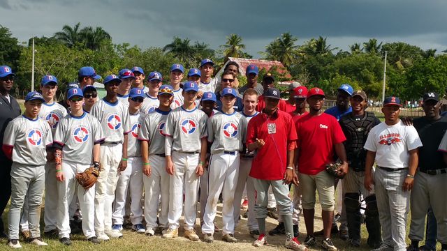 Team Avenue players and staff pose with a host team on a baseball field.